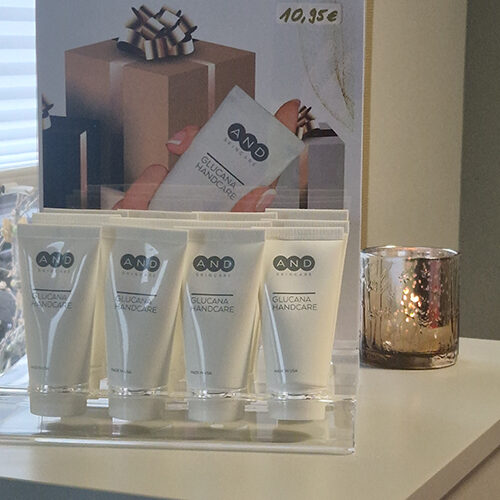 Handcreme Set von AND mit elegantem weißen Design und glänzender Kerze daneben