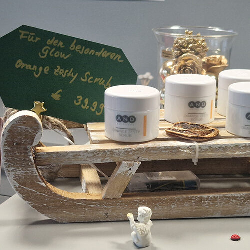 Vier weiße Cremedosen stehen auf einem rustikalen Holzschlitten mit grüner Tafel